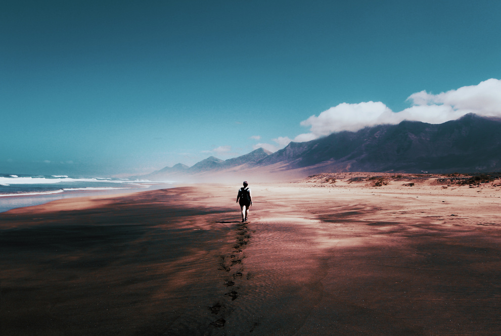 a person walking on the beach with mountains in the background